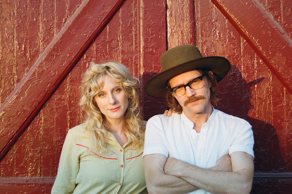 000094140026 Whitehorse - 2 piece band in country-style clothing standing against a red barn door