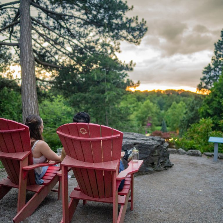 Couple seated in red muskoka chairs at sunset in the upper bowl of rock garden at RBG After Dark