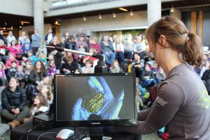 20180126 Frogs Exhibit Program Meet the Animals Toad McQuesten Theatre 002 Staff showing a large audience a green frog on a projector