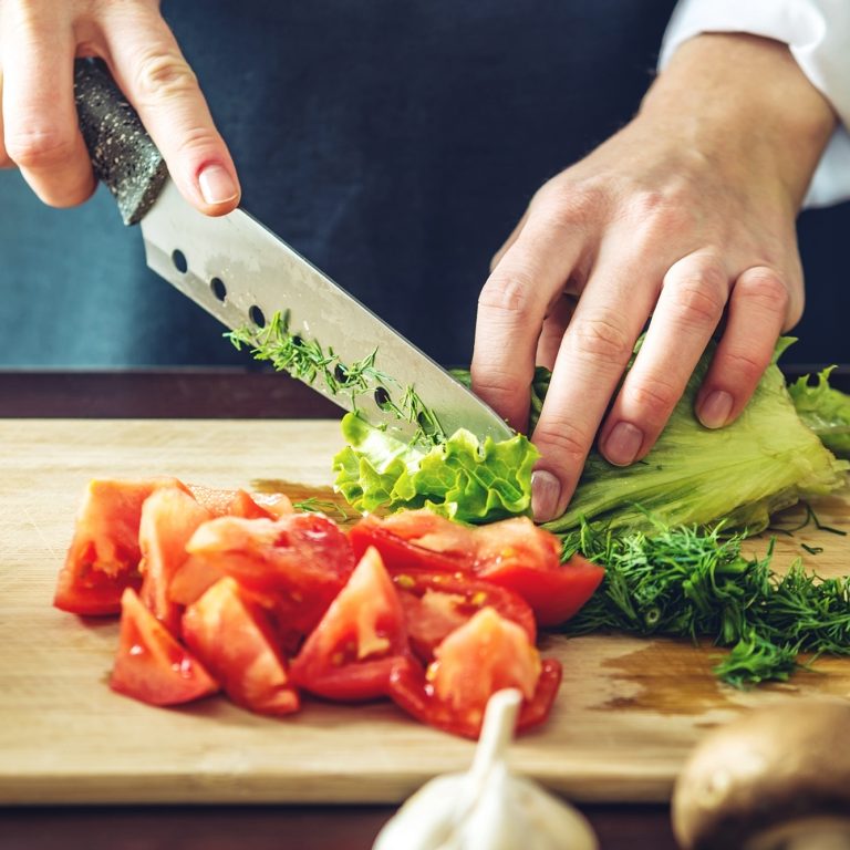 Chef Chopping tomatoes, lettuce and herbs on a cutting board