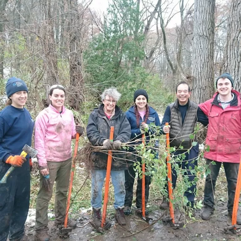 Volunteers Posing With Tools In Nature Sanctuary