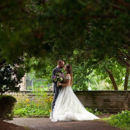 2021_Wedding_Hendrie_FotoFlarePhotography_243 Wedding couple posing under a dense canopy in a garden wedding venue