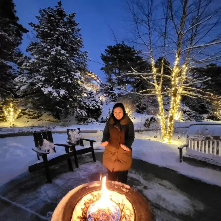 Person warming themselves in front of an outdoor firepit in the snowy lower bowl of the Rock Garden