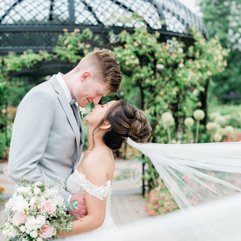 Bride and groom going for a kiss posing outdoors in a garden wedding venue in spring rose garden