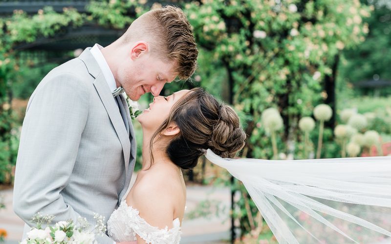 Bride and groom going for a kiss posing outdoors in a garden wedding venue in spring rose garden
