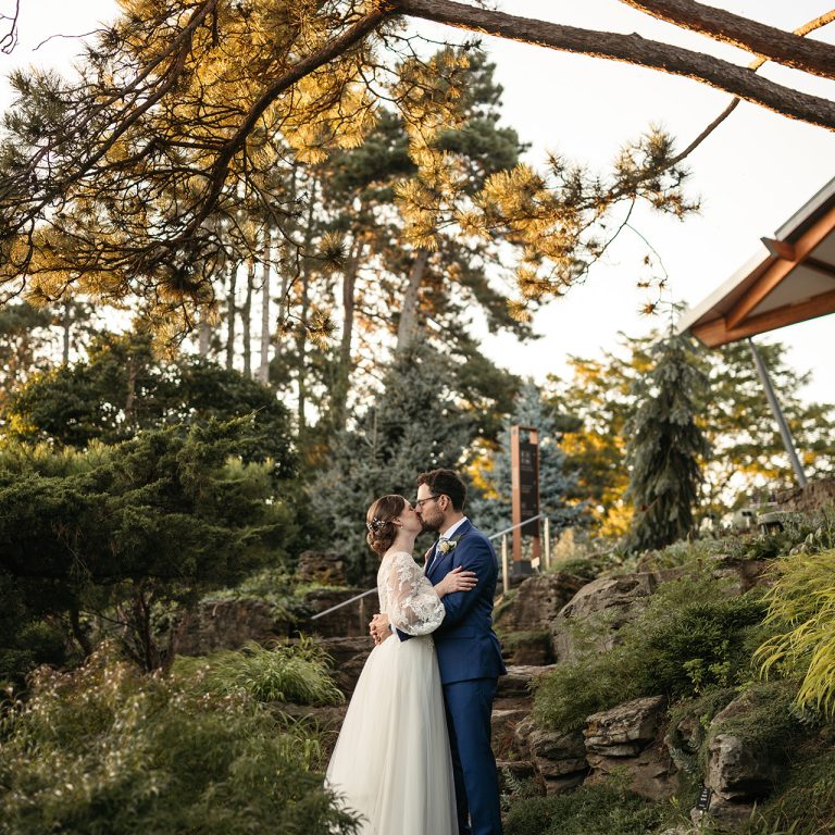 Bride and groom embracing along limestone steps in a summer rock garden wedding venue
