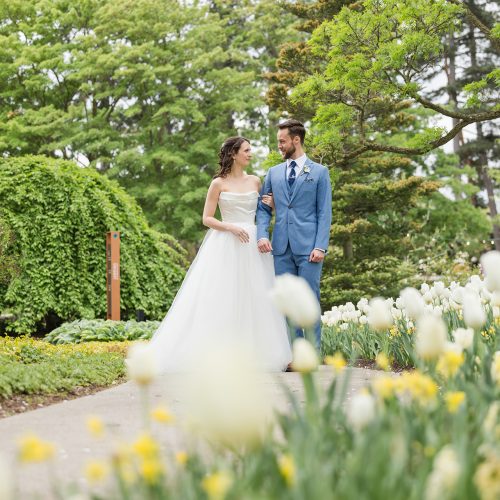 2025_Wedding_Rock_NicoleKirk_541 Bride and groom walking along curved pathway at Rock Garden, surrounded by tulip blooms
