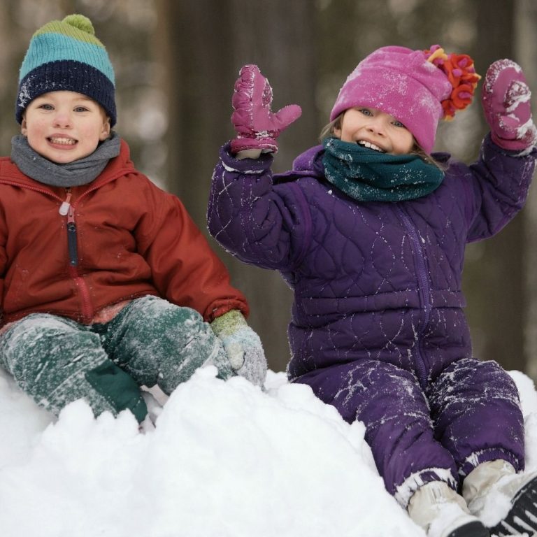 two young children dressed in winter snow attire sitting on a snow pile