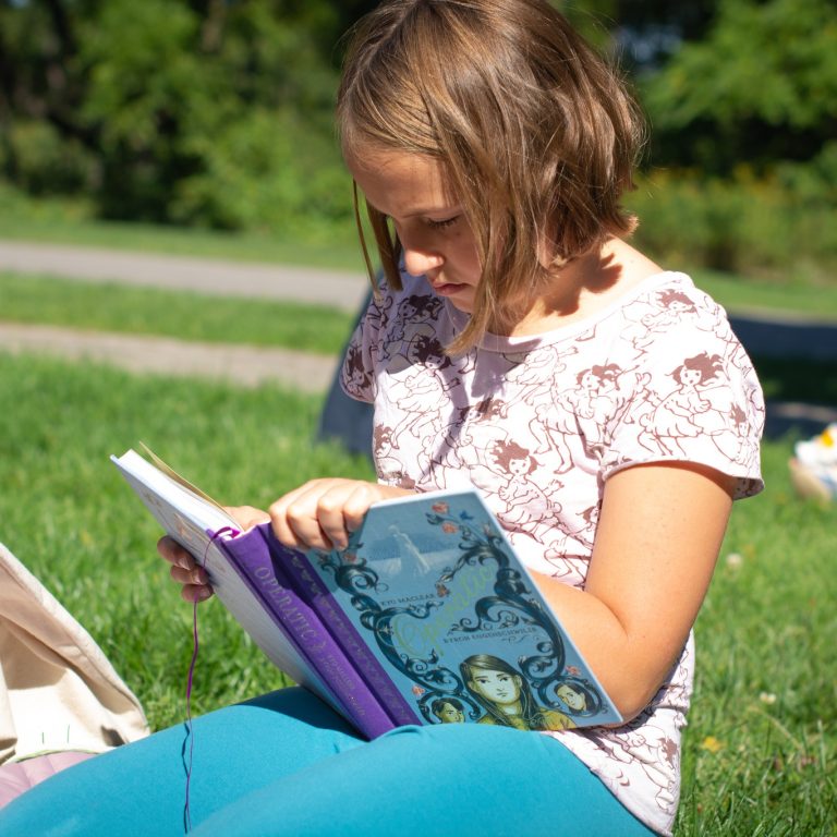 Child reading a book in the grass at Hendrie Park