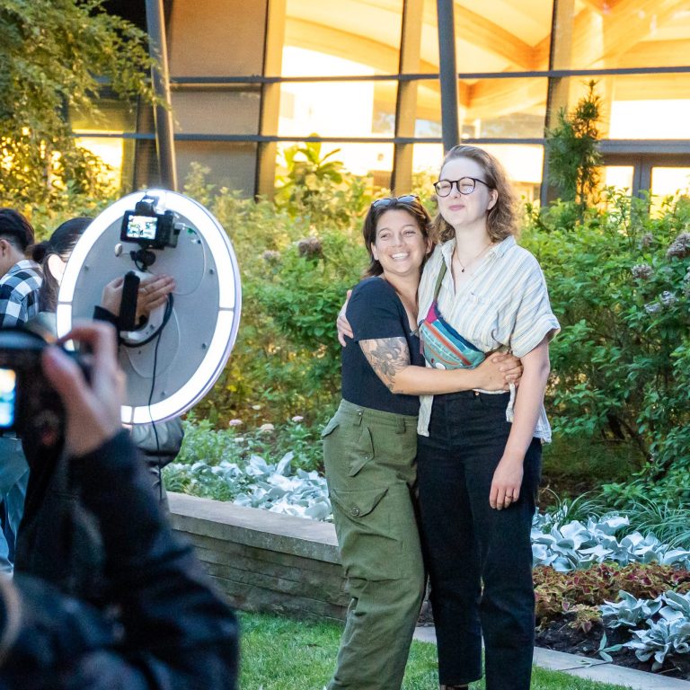 Two guests posing for a photo taken by a roaming photographer with a ring light.