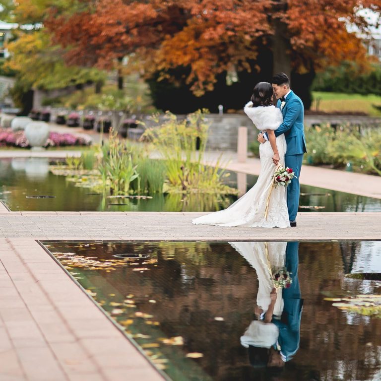 Bride and groom embracing at the edge of reflecting ponds, in fall