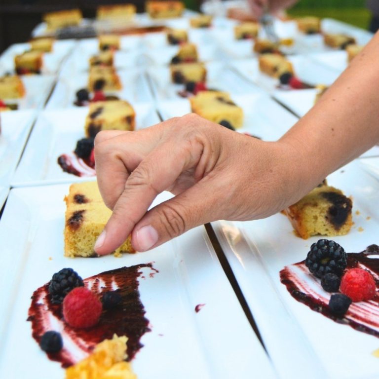 Hand prepping a large number of cake and berry desserts for a high-end meal