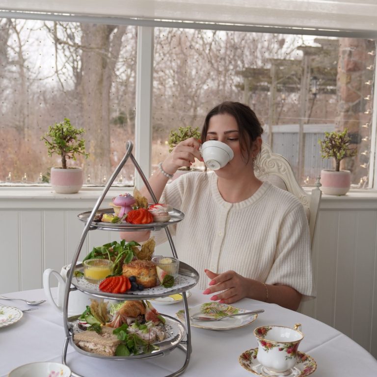 Guest sipping a cup of tea at the Tea House with a full tea platter in front of her