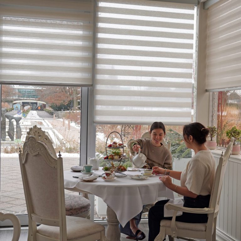 Two guests enjoying afternoon tea in the Tea House. One guest is pouring tea for the other guest