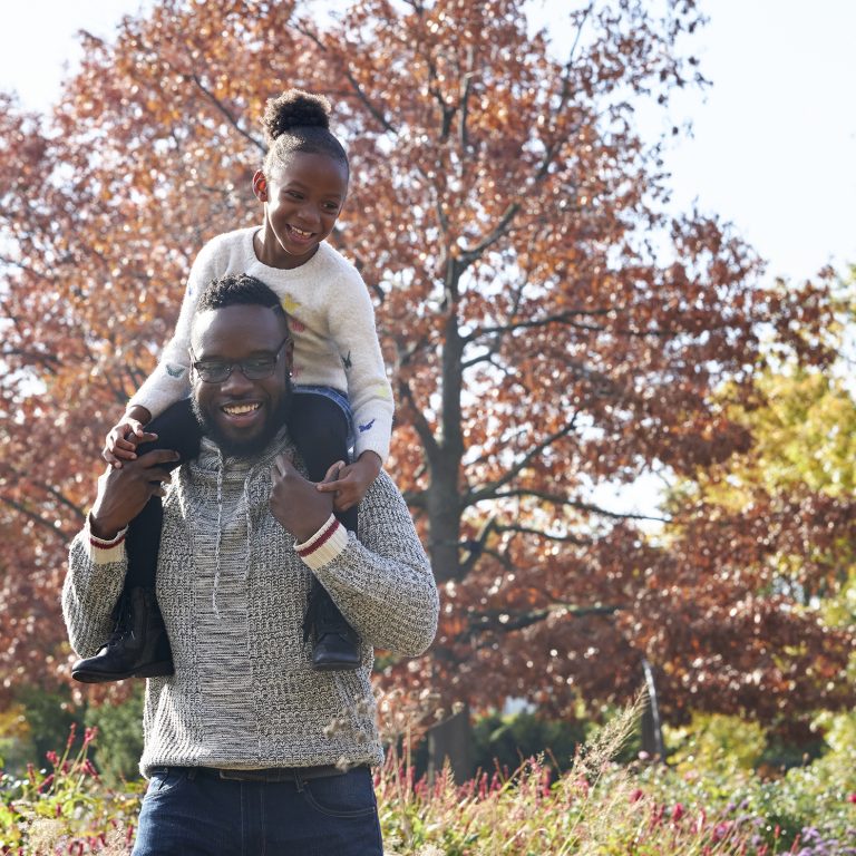 Father carrying daughter on shoulders in fall