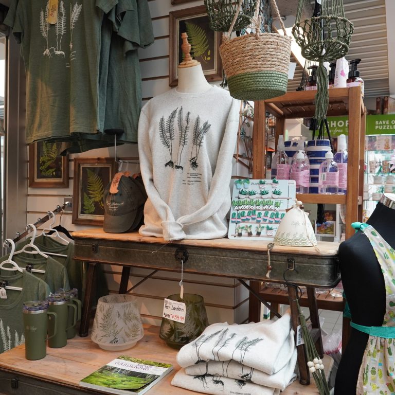 RBG brand merchandise displayed at the Garden Shop including tshirts, travel mugs, hats, and sweaters