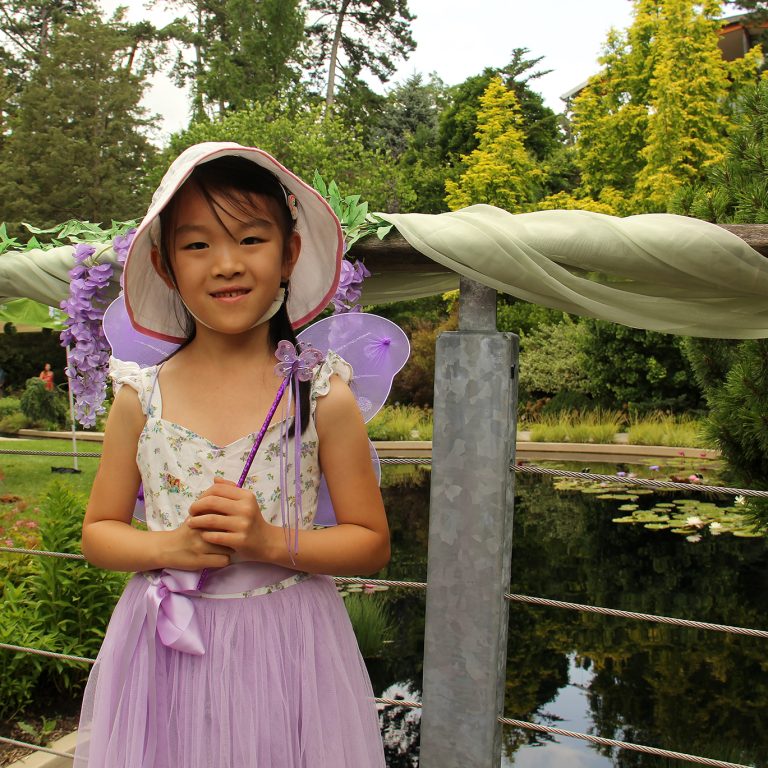 child dressed as a fairy on a garden bridge, holding a wand
