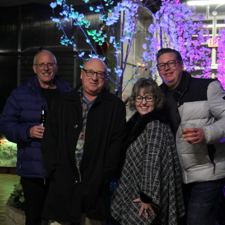 Four people posing together at After Dark in the evening with colorful illuminated flowering trees in the background