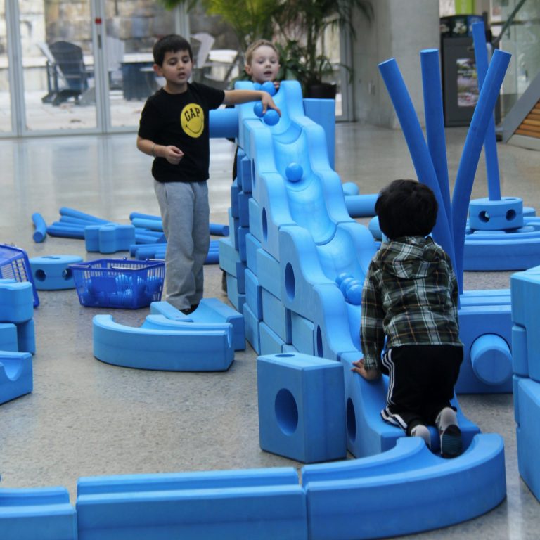 children playing and watching balls roll down a bumpy slide made of foam blocks and pieces