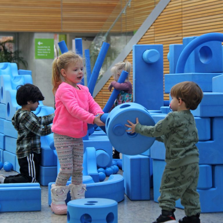 child passing circular foam piece to another while playing at the imagination playground