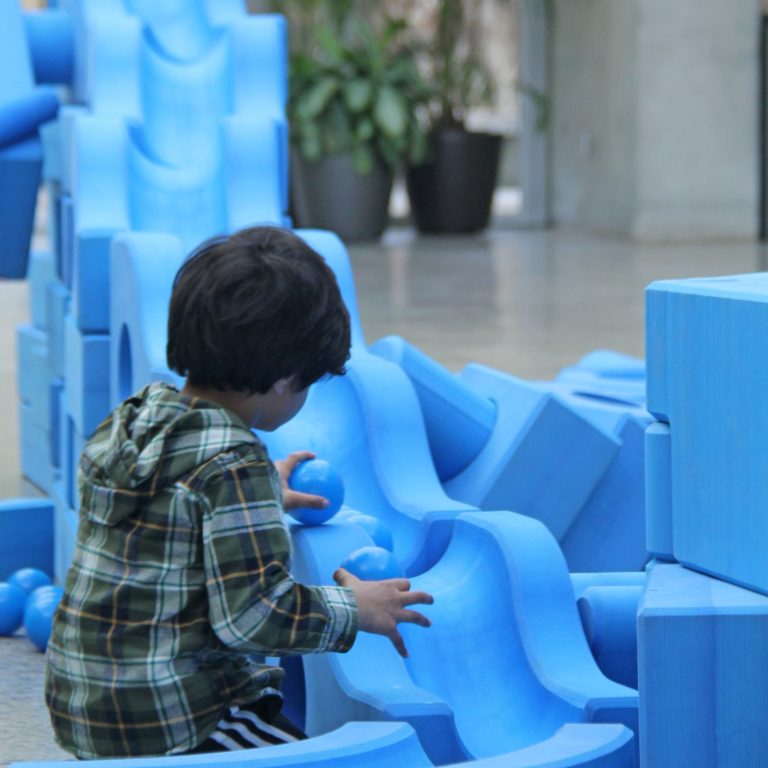 Child rolling plastic balls down a bumpy slide made of foam pieces