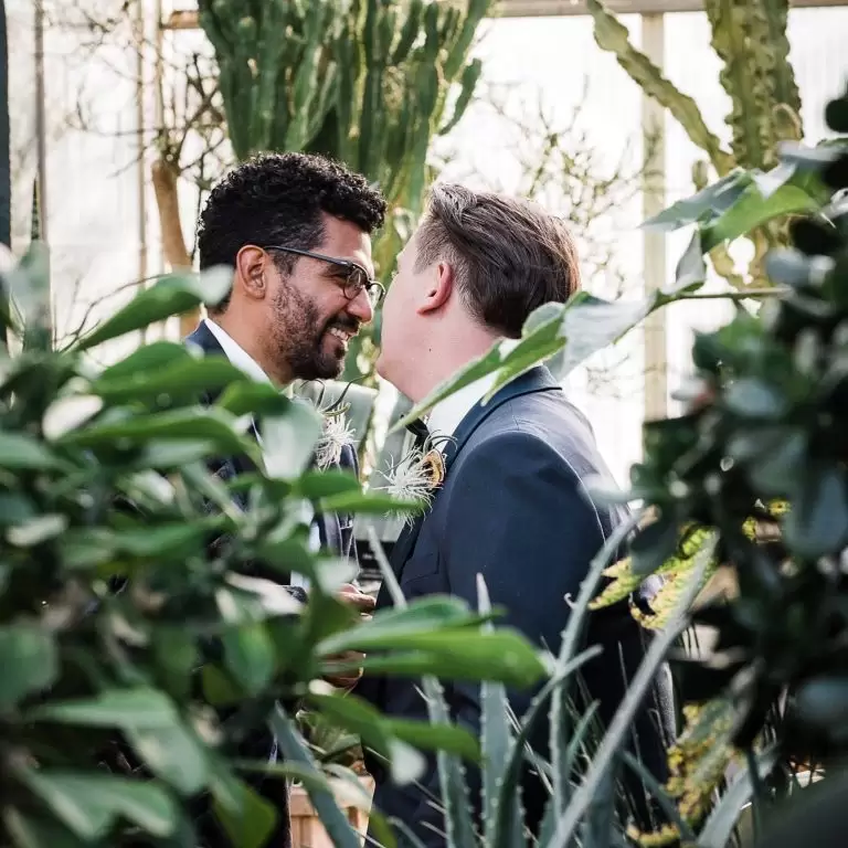 grooms romantically leaning towards each other in the Mediterranean garden