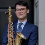 jacob chung wearing a blue suit and holding a saxophone