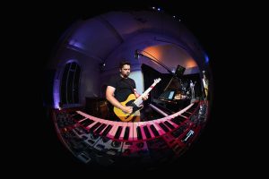 Michael Henley-Dunbar playing guitar and keyboard in dark performance space
