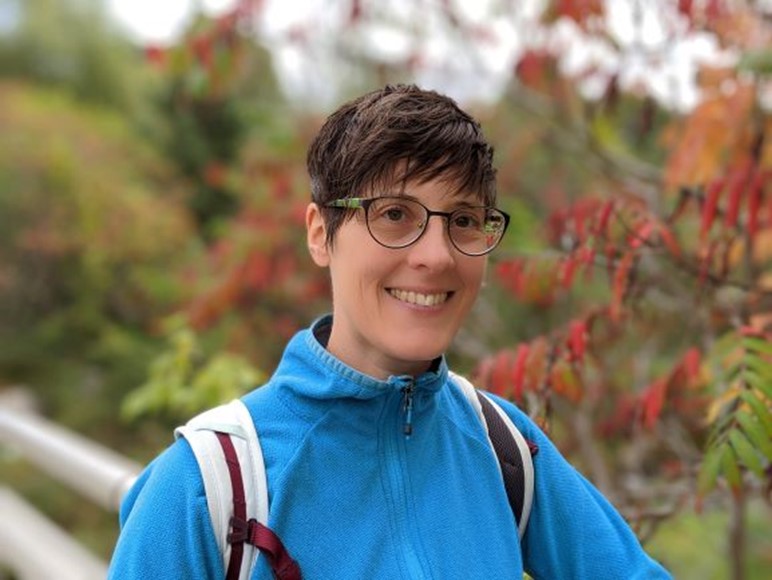 headshot of Nadia smiling while outdoors and wearing a blue jacket