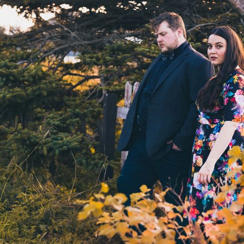 Quote the Raven Image Two individuals stand in a fall garden with solemn looks