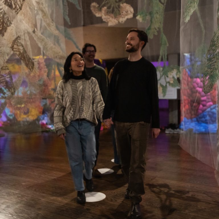 couple walking through tapestry with flowers embroidered on them