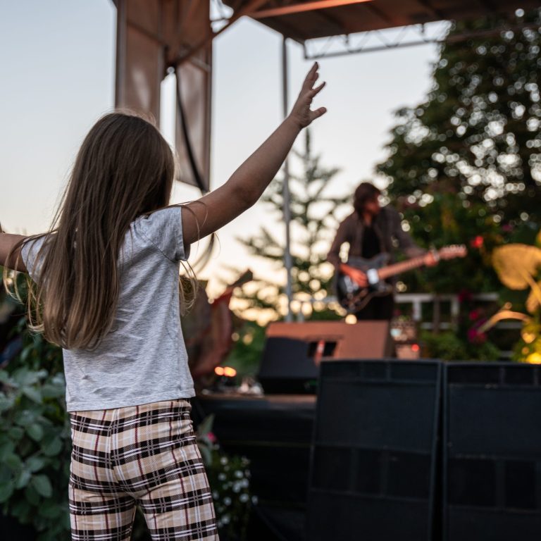 Child dancing in front of an outdoor stage with a band performing live music