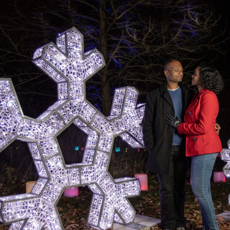 Couple looking at each other lovingly while posing in front of large snowflake light installations