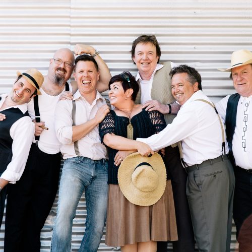 Western Swing Authority Credit_Christine Saunders Swing band stands against tin wall in folky clothing, tightly grouped together embracing