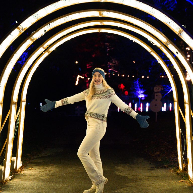 visitor [posing under an arch of lights at Winter Wonders