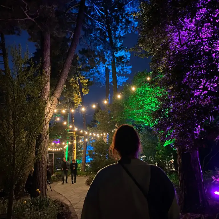 woman walking down lit garden pathway after dark