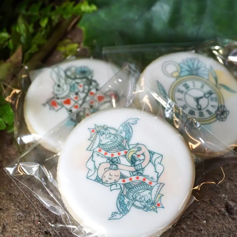 round cookies iced with white icing, printed with graphics depicting scenes from Alice's Adventures in Wonderland (Red Queen, March Hare, clock and florals)