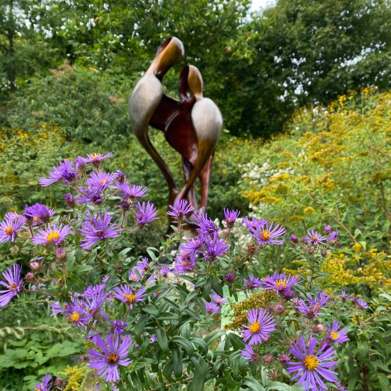 purple asters and goldenrod in front of a bronze sculpture