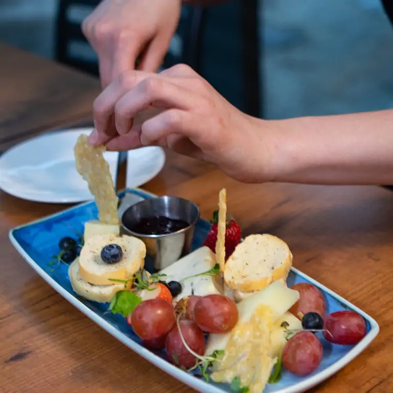 Hands preparing a cheese plate including fruites and crudites