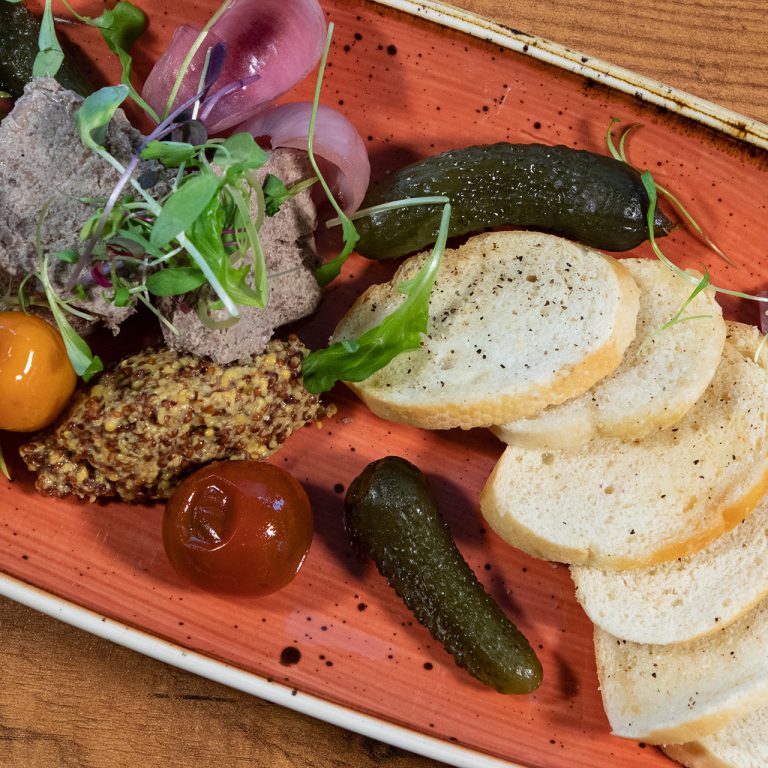 Chicken liver paté plated with baguette, mustard, pickles and other cruidites