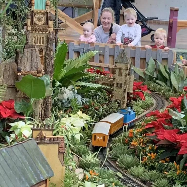 Children and parent watching a model Thomas the Tank engine moving through the botanical train display