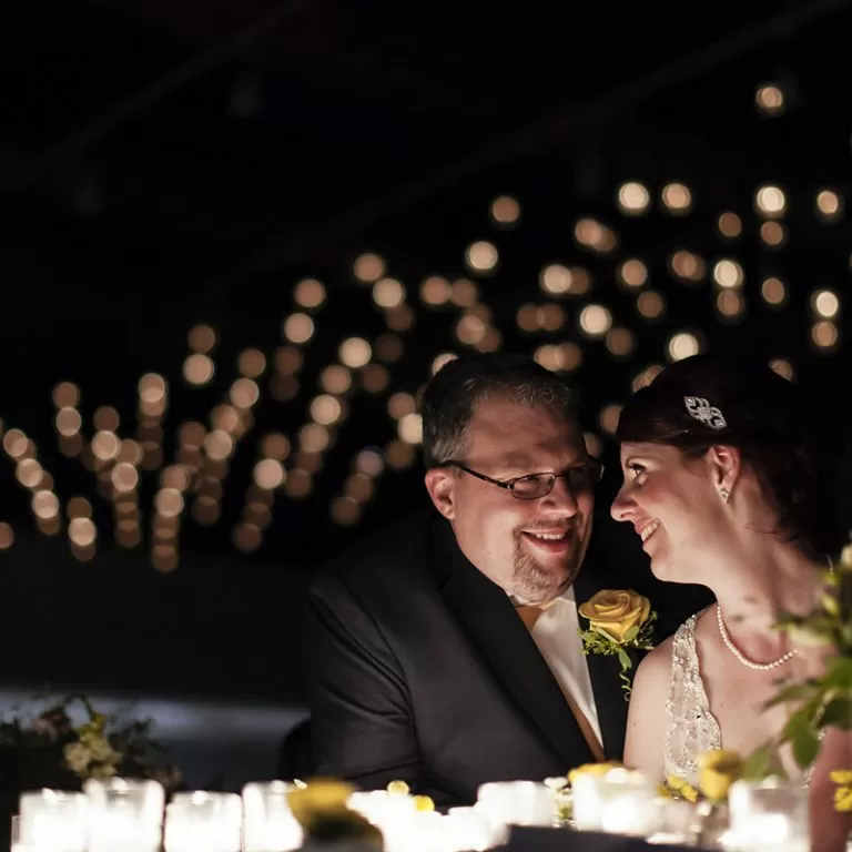 Bride and Groom sitting at table in dark reception hall with romantic lighting