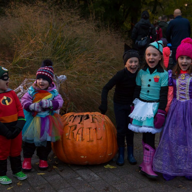 Children in costume standing around large carved pumpkin