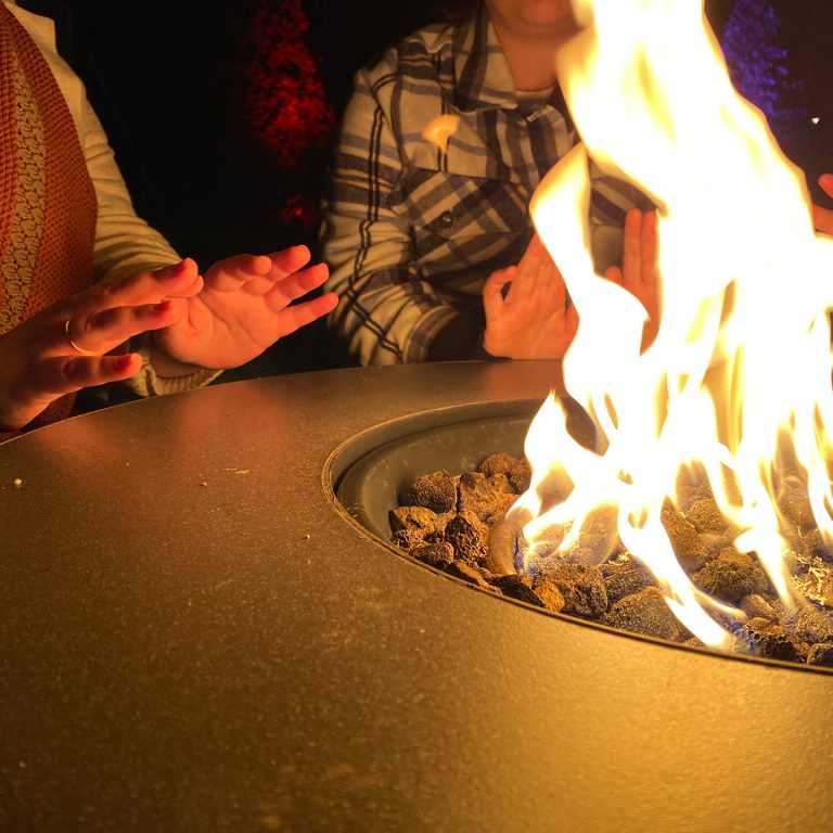 Two people warming hands by a high-end propane fire pit