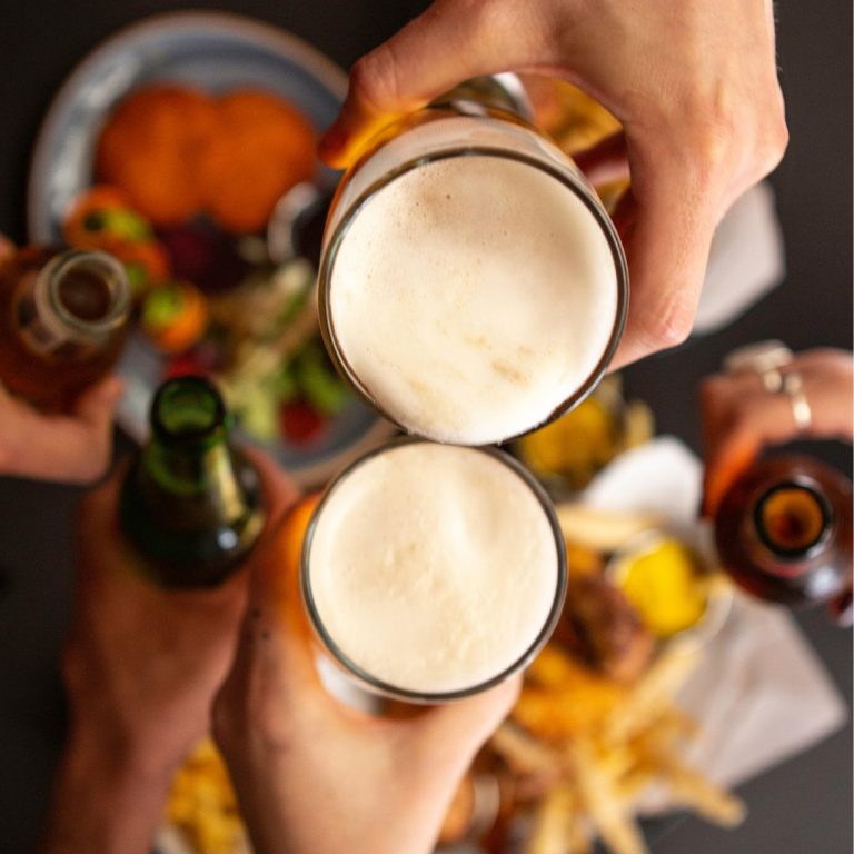 Cheers of draft and bottled beer over plates of fries, burgers, and other food