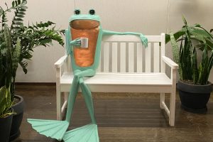 frog-bench-sculpture painted bronze frog statue sitting on white bench and holding a coffee cup