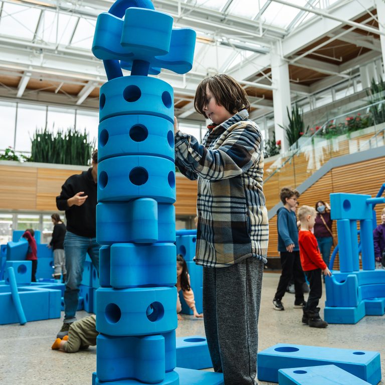 child constructing a large tower from foam blocks