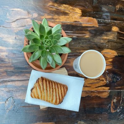 Pastry and coffee - Greenhouse Cafe Cup of coffee and pastry laid flat on a wooden table next to a succulent