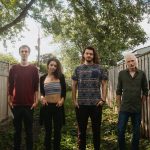 Four people standing outdoors in a small fenced in yard