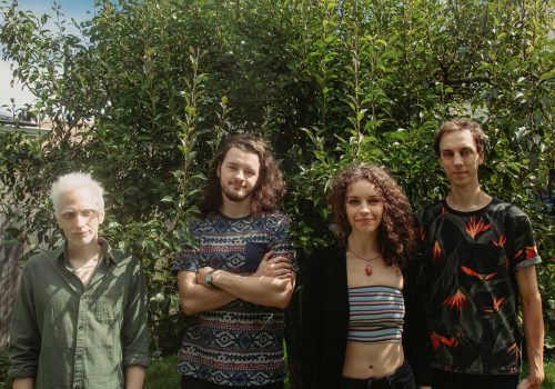 junestone_og5 4 members of the Junestone musician group standing in front of a large bush on a bright summer day, dressed casually